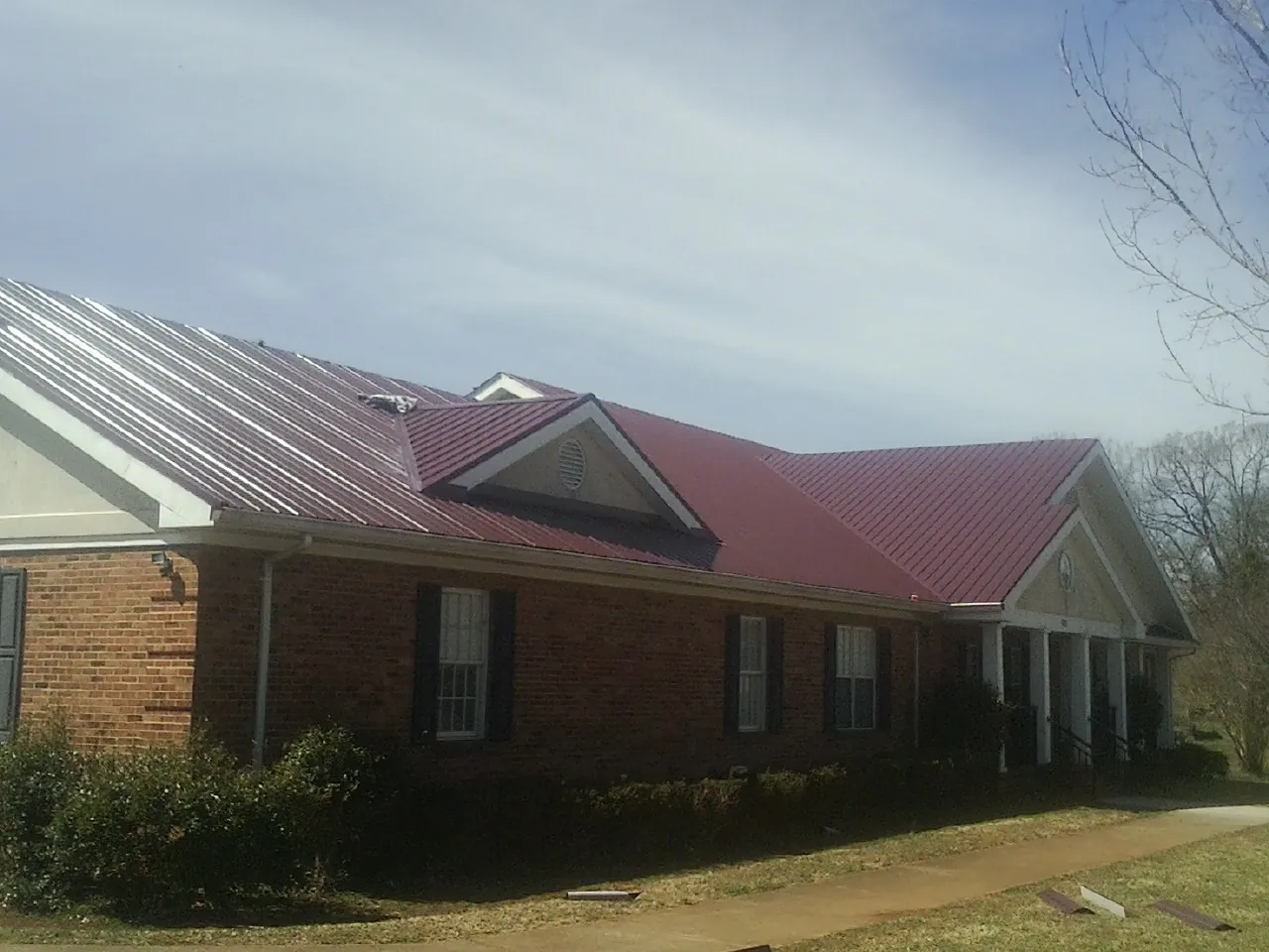 Red metal roof with gabled entries on a long brick building, from a Hail Damage Roof Repair job in New Lisbon