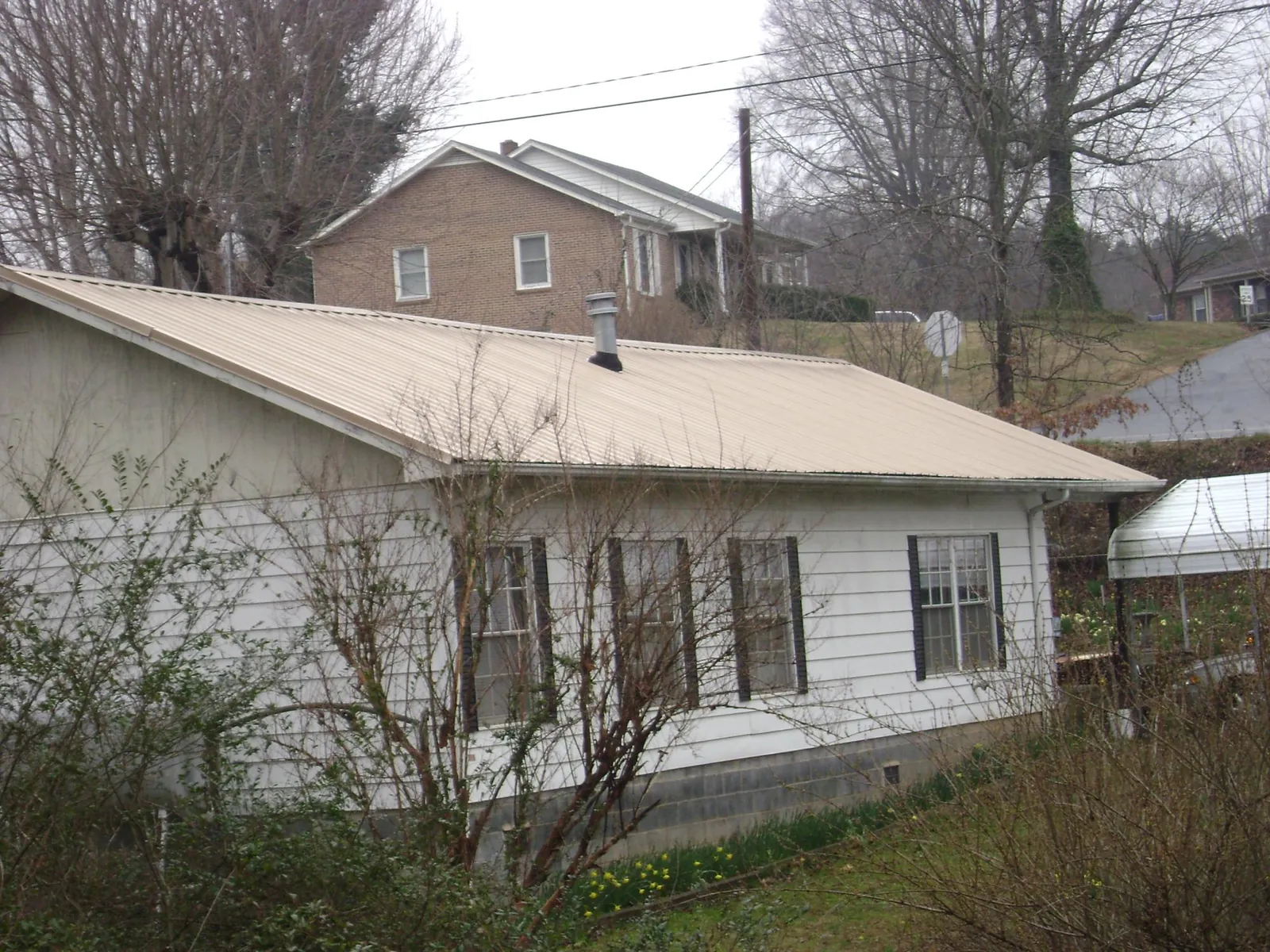 Tan metal roof on a white sided house set into a hillside — Commercial Roofing by Roofing Brothers in New Lisbon